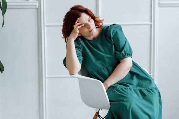 Woman in Green Dress Sitting on a Chair while in Deep Thoughts